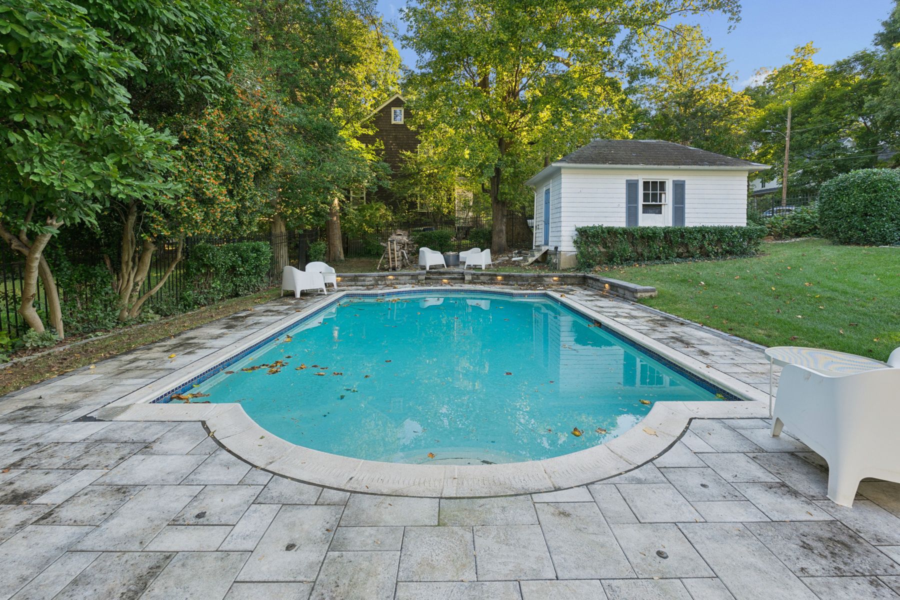In-ground pool with stone patio, low lit seat wall and the detached one-car garage