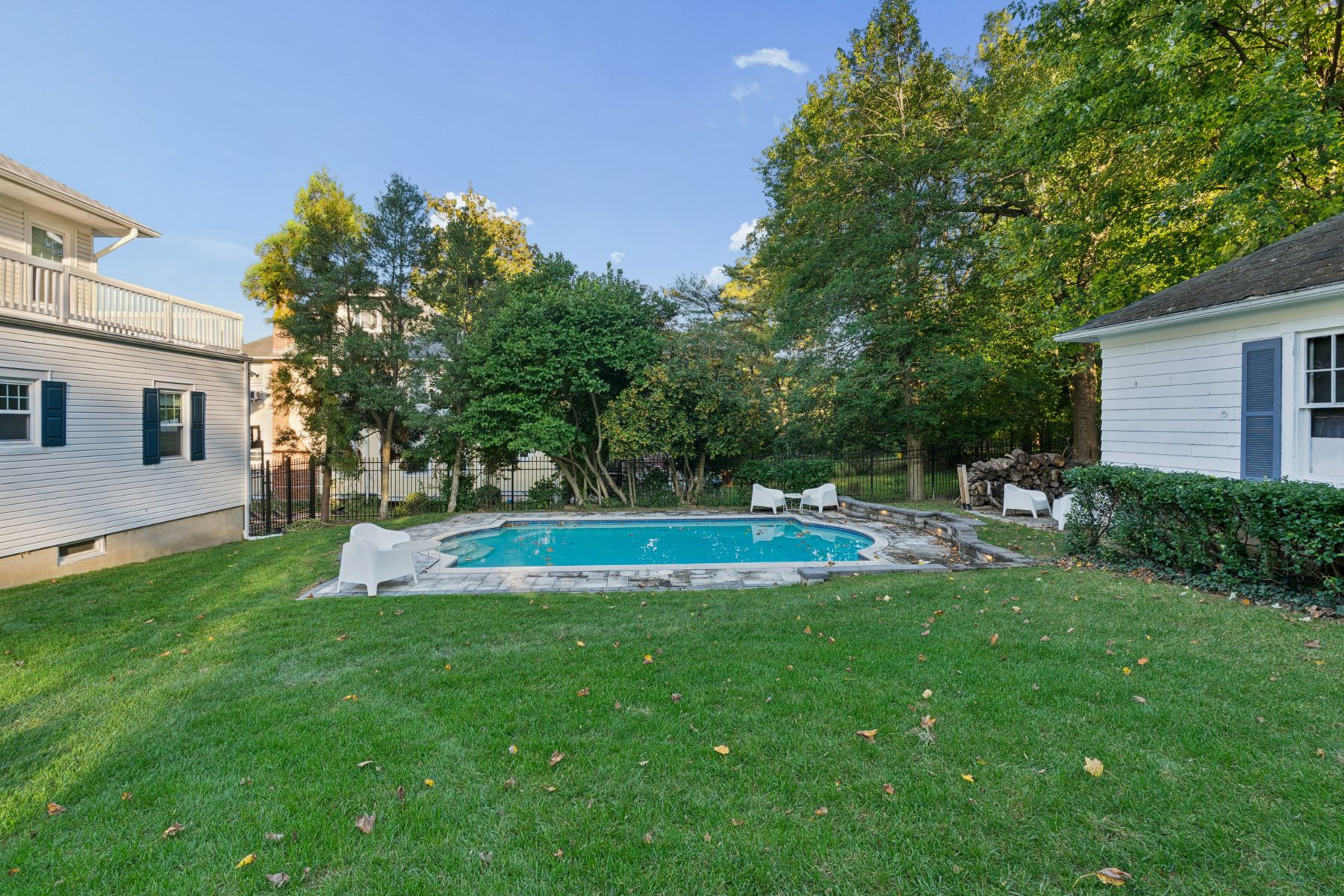 Lawn leading to the pool, framed by mature trees and an iron fence